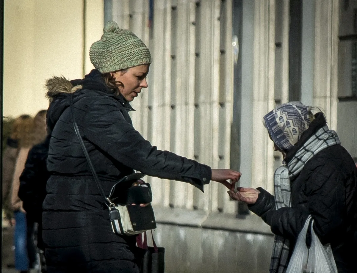 Woman dropping a coin into another woman's open hand on a city street